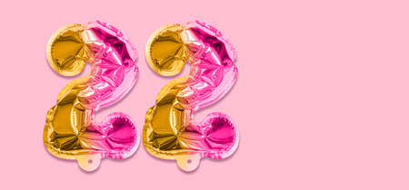 Rainbow foil balloon number, digit twenty two on a pink background. Birthday greeting card with inscription 22. Top view. Numerical digit. Celebration event template. Banner.の写真素材