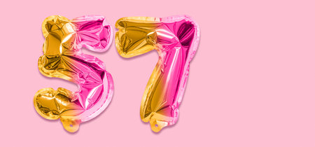 Rainbow foil balloon number, digit fifty seven on a pink background. Birthday greeting card with inscription 57. Top view. Numerical digit. Celebration event template. Banner.の写真素材