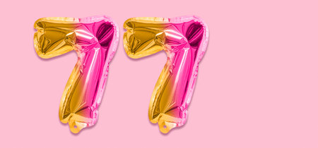 Rainbow foil balloon number, digit seventy seven on a pink background. Birthday greeting card with inscription 77. Top view. Numerical digit. Celebration event template. Banner.の写真素材