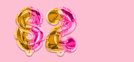 Rainbow foil balloon number, digit eighty two on a pink background. Birthday greeting card with inscription 82. Top view. Numerical digit. Celebration event template. Banner.の写真素材