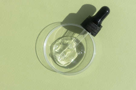 Hyaluronic acid serum or gel for the face with a pipette in Petri dish on a green background. Concept of cosmetics laboratory researches, wellness and beauty.の写真素材