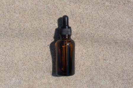 A bottle of dark amber glass with gel or serum with hyaluronic acid on the sand. natural organic cosmetics. Layout of the beauty salon branding. top viewの写真素材
