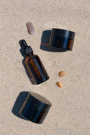 Bottles of dark amber glass with gel, serum with hyaluronic acid and face cream on the sand. Natural SPA organic cosmetic. Layout of the beauty salon branding. top viewの写真素材