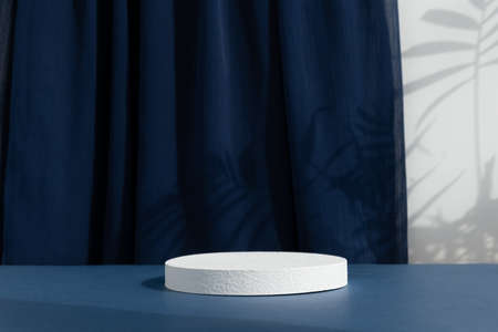 White cylindrical podium, pedestal on a blue background with curtain and palm shadow. Scene for the presentation of a cosmetic product. empty showcase.の写真素材