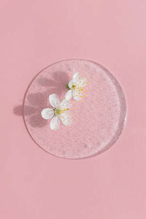 A drop of transparent cosmetic gel or serum with white flowers on a pink background. The concept of natural cosmetics. top view.の写真素材