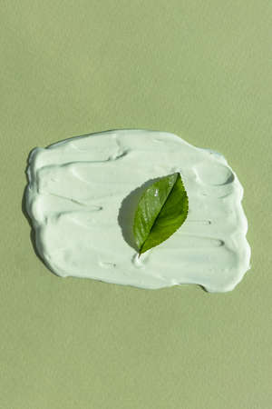 The texture of the cream with a green leaf on a green background. Smear of skincare cosmetics...