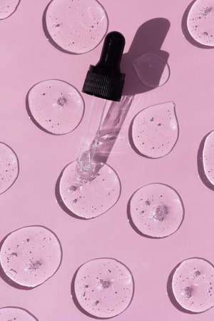Drops of serum or hyaluronic acid gel with a pipette on a pink background. Smears of cosmetic skin care products. wellness and beauty concept.の写真素材