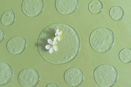 Drops of transparent cosmetic gel or serum with white flowers on a green background. The concept of natural cosmetics. top view.の写真素材