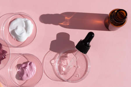 Multicolored texture of cream, scrub and gel in a Petri dish with a pipette and a bottle on a pink background. The concept of laboratory research of cosmetics. Smears of cosmetic skin care products.の写真素材