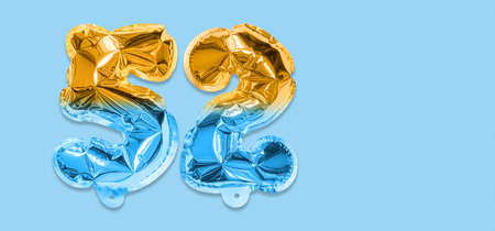 Rainbow foil balloon number, digit fifty two on a blue background. Birthday greeting card with inscription 52. Top view. Numerical digit. Celebration event template. Bannerの写真素材