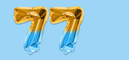 Rainbow foil balloon number, digit seventy seven on a blue background. Birthday greeting card with inscription 77. Top view. Numerical digit. Celebration event template. Bannerの写真素材