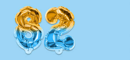 Rainbow foil balloon number, digit eighty two on a blue background. Birthday greeting card with inscription 82. Top view. Numerical digit. Celebration event template. Bannerの写真素材