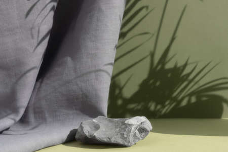 A podium made of natural stone on a green background with a gray curtain and a shadow of palm leaves. Showcase for product promotion, beauty, natural eco cosmetic. copyspace.の写真素材