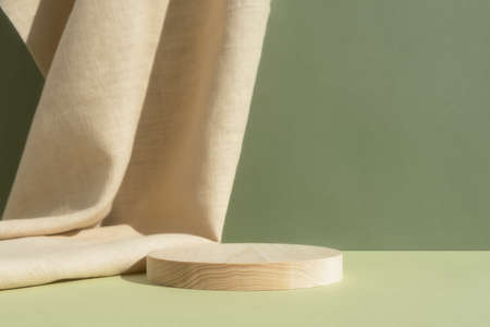 Wooden cylindrical podium, pedestal on a green background with beige curtain. Scene for the presentation of a cosmetic product. empty showcaseの写真素材