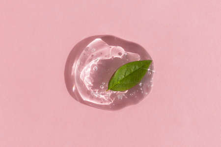 A drop of transparent cosmetic gel or serum with hyaluronic acid with a green leaf on a pink background. The concept of natural cosmetics. top view.の写真素材