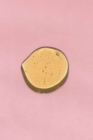 The texture of serum, oil, hyaluronic acid or gel on a pink background. A drop of yellow cosmetic product. wellness and beauty concept.の写真素材