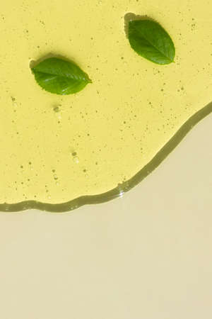 Transparent cosmetic gel or serum of yellow color with green leaves on a light beige background. The concept of natural cosmetics. Top view.の写真素材