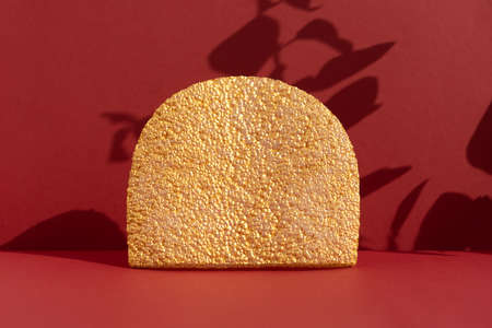 Geometric golden podium on an abstract burgundy background with a shadow of plant leaves. Scene for the product presentation. Showcase, display caseの写真素材