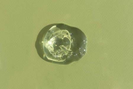 A drop of transparent cosmetic gel or serum with hyaluronic acid on a green background. wellness and beauty concept. top view.の写真素材
