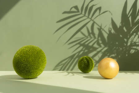 Minimal abstract scene with grass and golden balls with the shadow of palm leaves on a green background. Premium podium for product promotion, beauty, natural eco cosmetic. Showcase, display case.の写真素材