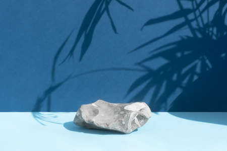 The podium is made of gray stone on a blue background with a shadow from the leaves of a palm tree. Scene for product promotion, beauty, natural eco cosmetic. Showcase, display case.の写真素材