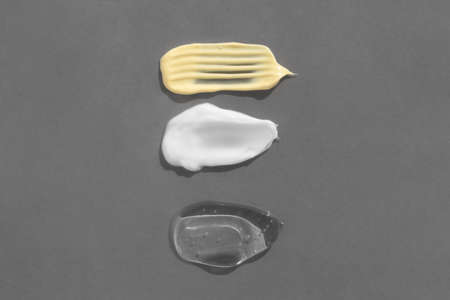 Smears of yellow, white cream and transparent gel or serum on a gray background. The texture of a cosmetic skin care product. top view.の写真素材