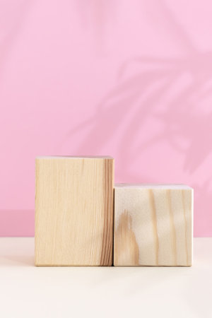 Wooden podiums, pedestals on a pink background with a shadow of tropical palm leaves. Showcases for the promotion of products, beauty, natural cosmetics on a beige table.の写真素材