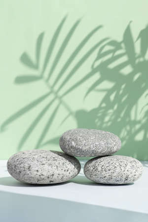 A podium made of stones on a gray table against a green wall with a shadow from the leaves of a palm tree. Showcase for product promotion, beauty, natural cosmeticsの写真素材