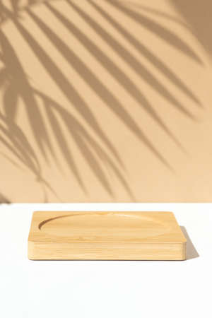 Minimal abstract background for the presentation of a cosmetic product. Wooden scene on a white table. Premium podium with a shadow of tropical palm leaves on a beige wall. Show case, display case.の写真素材