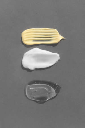 Smears of yellow, white cream and transparent gel or serum on a gray background. The texture of a cosmetic skin care product. top view.の写真素材