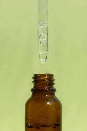A bottle of dark amber glass with a serum or gel with a pipette on a green background. Cosmetic product with hyaluronic acid. front view.の写真素材