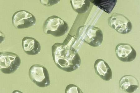Drops of liquid gel or serum with a pipette on a green background. The texture of a cosmetic product with oxygen bubbles. wellness and beauty concept.の写真素材