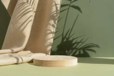 Wooden cylindrical podium, pedestal on a green background with beige curtain and a shadow of palm leaves. Scene for the presentation of a cosmetic product. empty showcaseの写真素材