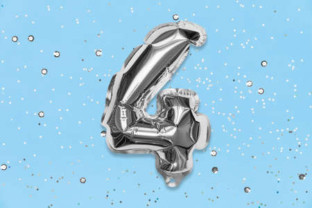 Silver foil balloon number, digit four on a blue background with sequins. Birthday greeting card with inscription 4. Top view. Numerical digit. Celebration event, template.の写真素材