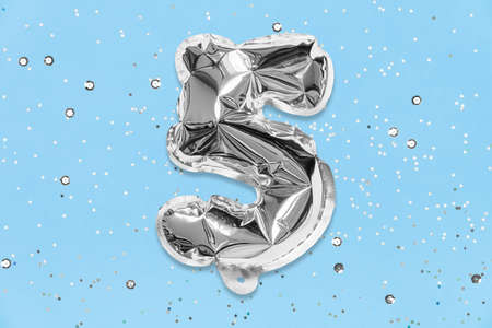 Silver foil balloon number, digit five on a blue background with sequins. Birthday greeting card with inscription 5. Anniversary concept. Top view. Numerical digit. Celebration event, template.の写真素材