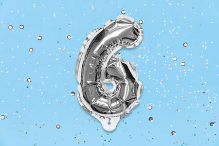 Silver foil balloon number, digit six on a blue background with sequins. Birthday greeting card with inscription 6. Top view. Numerical digit. Celebration event, template.の写真素材