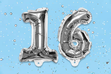 Silver foil balloon number, digit sixteen on a blue background with sequins. Birthday greeting card with inscription 16. Anniversary concept. Top view. Numerical digit. Celebration event, template.の写真素材