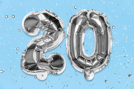 Silver foil balloon number, digit twenty on a blue background with sequins. Birthday greeting card with inscription 20. Anniversary concept. top view. Numerical digit. Celebration event template.の写真素材