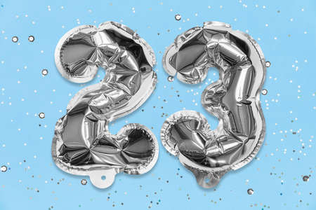 Silver foil balloon number, digit twenty three on a blue background with sequins. Birthday greeting card with inscription 23. Top view. Numerical digit. Celebration event, template.の写真素材