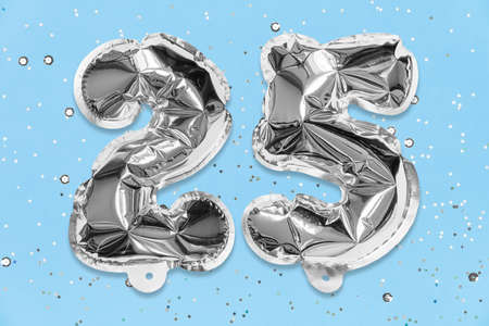 Silver foil balloon number, digit twenty five on a blue background with sequins. Birthday greeting card with inscription 25. Anniversary concept. Numerical digit. Celebration event, template.の写真素材