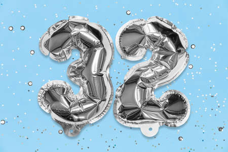 Silver foil balloon number, digit thirty two on a blue background with sequins. Birthday greeting card with inscription 32. Top view. Numerical digit. Celebration event, template.の写真素材