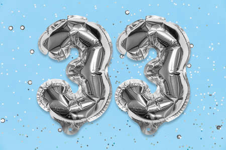 Silver foil balloon number, digit thirty three on a blue background with sequins. Birthday greeting card with inscription 33. Top view. Numerical digit. Celebration event, template.の写真素材