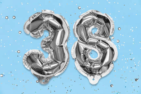 Silver foil balloon number, digit thirty eight on a blue background with sequins. Birthday greeting card with inscription 38. Top view. Numerical digit. Celebration event, template.の写真素材
