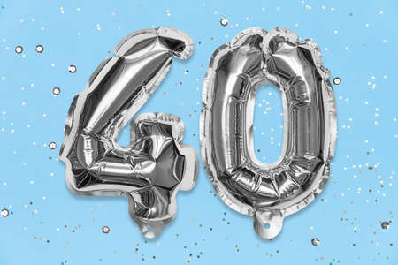 Silver foil balloon number, digit forty on a blue background with sequins. Birthday greeting card with inscription 40. Anniversary concept. top view. Numerical digit. Celebration event template.の写真素材