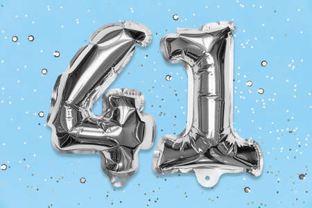 Silver foil balloon number, digit forty one on a blue background with sequins. Birthday greeting card with inscription 41. Top view. Numerical digit. Celebration event, template.の写真素材