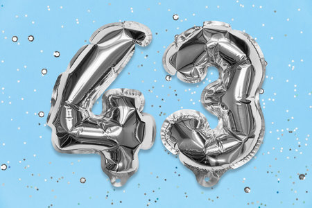 Silver foil balloon number, digit forty three on a blue background with sequins. Birthday greeting card with inscription 43. Top view. Numerical digit. Celebration event, template.の写真素材