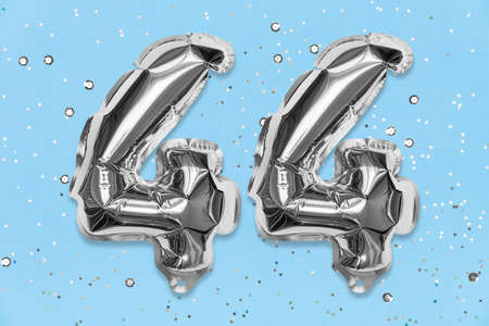 Silver foil balloon number, digit forty four on a blue background with sequins. Birthday greeting card with inscription 44. Top view. Numerical digit. Celebration event, template.の写真素材