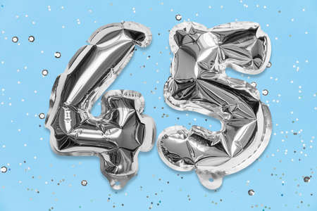 Silver foil balloon number, digit forty five on a blue background with sequins. Birthday greeting card with inscription 45. Anniversary concept. Numerical digit. Celebration event template.の写真素材