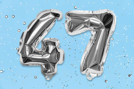 Silver foil balloon number, digit forty seven on a blue background with sequins. Birthday greeting card with inscription 47. Top view. Numerical digit. Celebration event, template.の写真素材