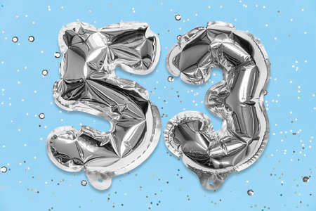 Silver foil balloon number, digit fifty three on a blue background with sequins. Birthday greeting card with inscription 53. Top view. Numerical digit. Celebration event, template.の写真素材